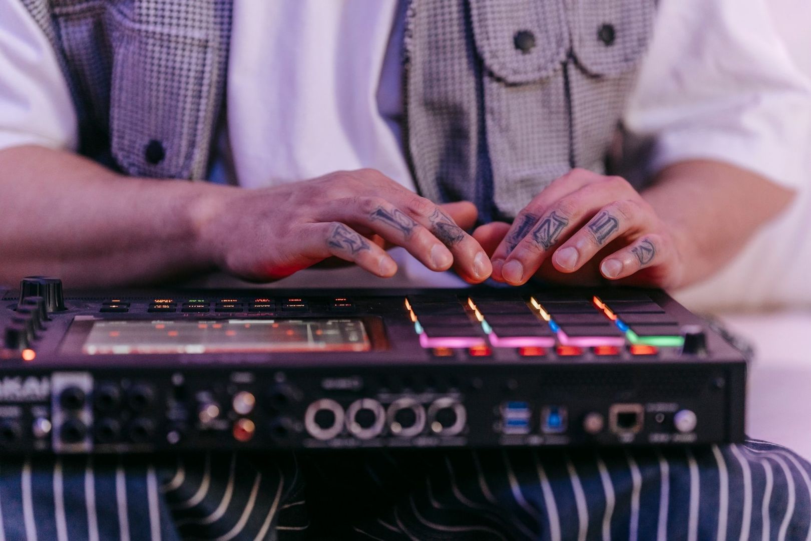 Tätowierte Hände bedienen eine beleuchtete Drum-Machine für elektronische Grooves
